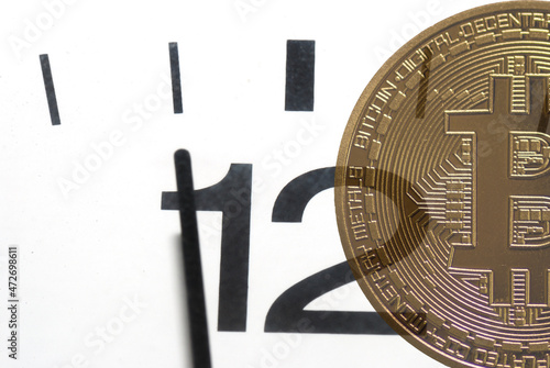 golden value bitcoin and a clock 5 minutes before twelve on white