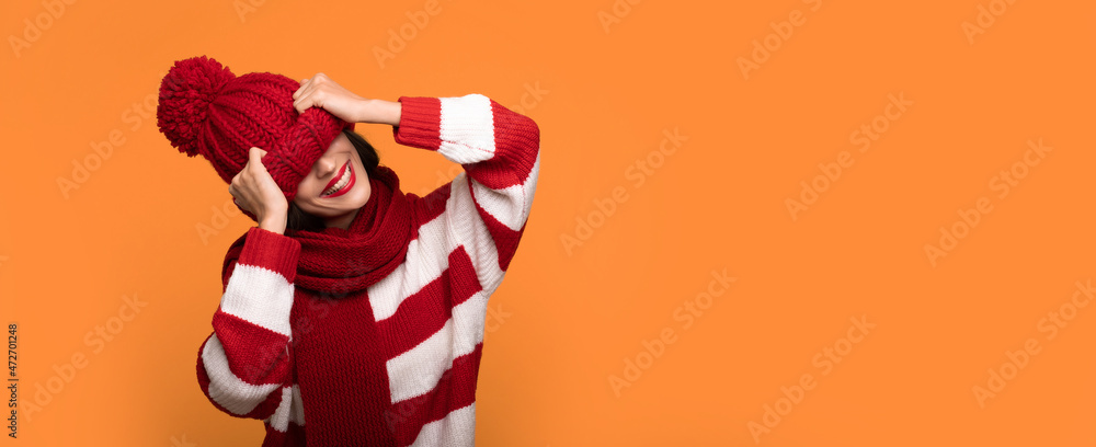 Banner photo of Excited funny young smiling girl is covering her face with help of big red winter hat while posing on yellow background Banner photo of Excited funny young smiling girl is covering her face with help of big red winter hat while posing on yellow background