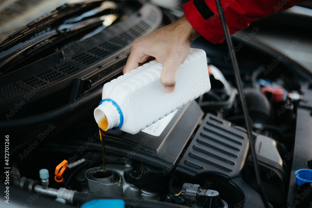 Close up photo of a male mechanic hand while he changes and pouring oil quality into the engine of the hybrid motor car. Maintenance Gear concept of auto in repair service Close up photo of a male mechanic hand while he changes and pouring oil quality into the engine of the hybrid motor car. Maintenance Gear concept of auto in repair service