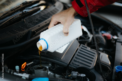 Close up photo of a male mechanic hand while he changes and pouring oil quality into the engine of the hybrid motor car. Maintenance Gear concept of auto in repair service