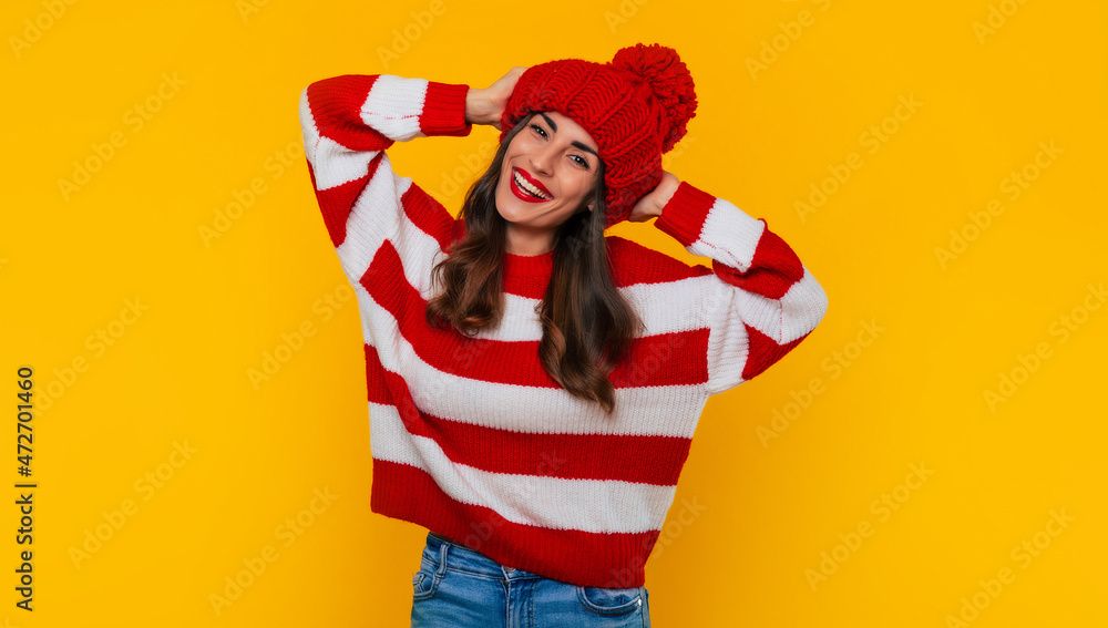 Close up photo of a beautiful happy brunette woman in red winter hat and scarf and posing isolated on yellow background