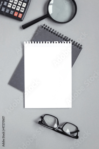 blank notebook on gray background near magnifier of glasses calculator