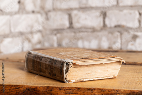 An old book in a battered binding lies against a brick wall made of light brick. Close-up, selective focus
