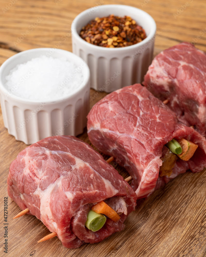 Rolled beef or roulade, vegetable and bacon stuffed meat over wooden table with seasonings Rolled beef or roulade, vegetable and bacon stuffed meat over wooden table with seasonings
