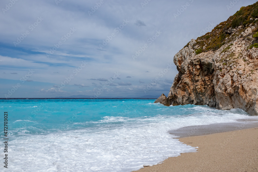 Azure vibrant stormy waves breaking rocky coast. Mylos sandy beach with dramatic cloudy sky on Lefkada island in Greece. Summer nature travel to Ionian Sea
