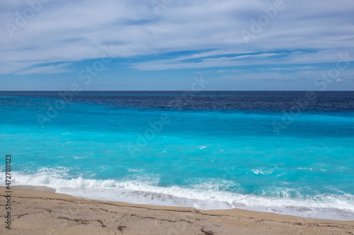 Azure vibrant waves with blue sky on sunny coast of Greek island. Sandy beach in Greece. Summer nature vacation travel to Ionian Sea
