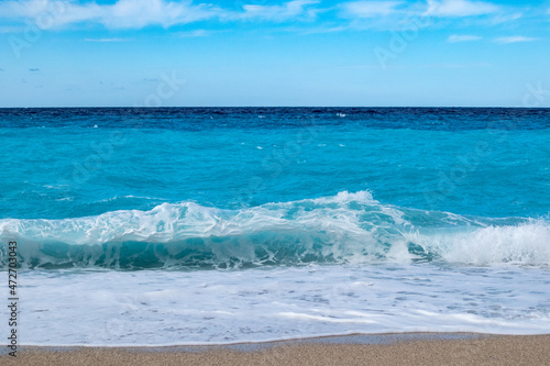 Azure vibrant breaker waves hitting shore of Greek island with blue sky. Sandy beach in Greece. Summer nature travel to Ionian Sea