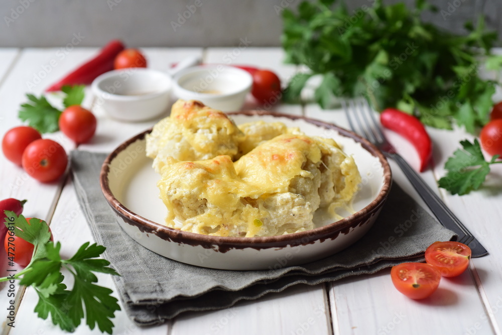 A hearty lunch for the family: cauliflower baked in cream sauce with cheese on a white plate on a white table. Close-up