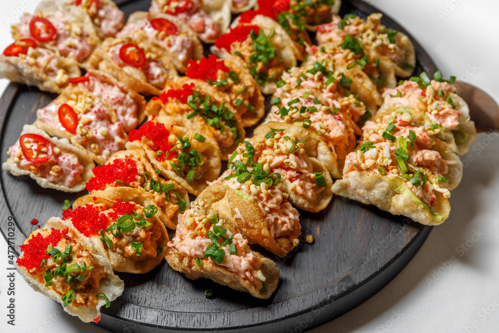 Potato chips with meat filling and decorated with caviar, onion, bell pepper on a wooden tray.