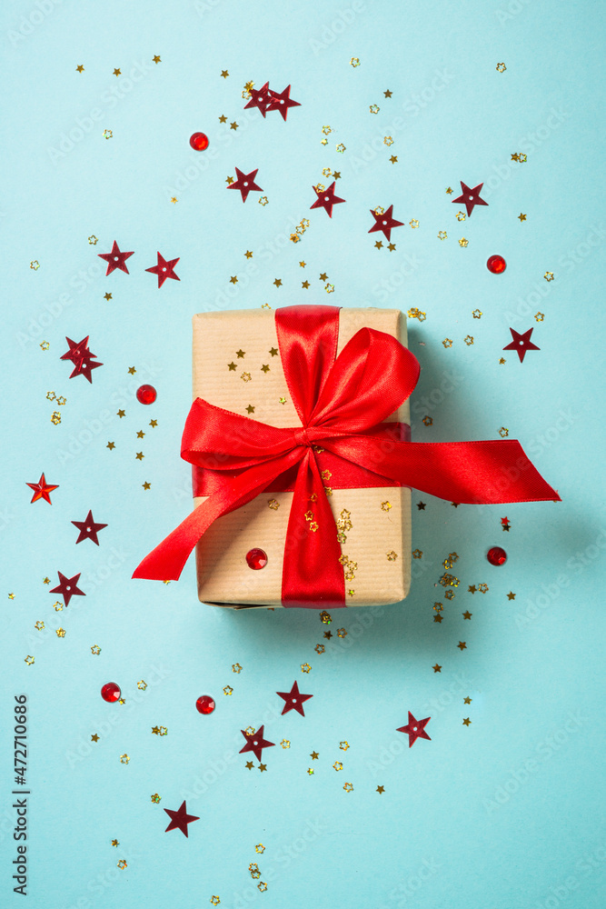 Christmas present box with red ribbon and glitter. Flat lay image on blue. Christmas present box with red ribbon and glitter. Flat lay image on blue.