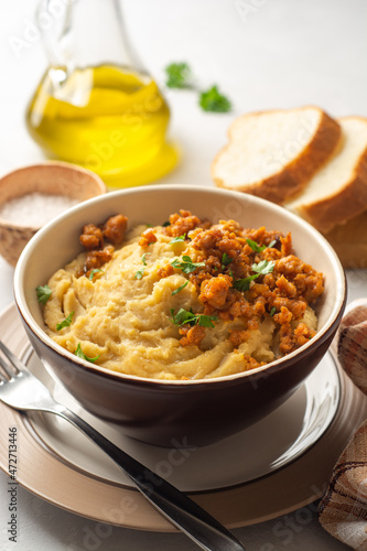 Yellow pea puree or porridge or pudding with meat sauce in bowl on concrete background