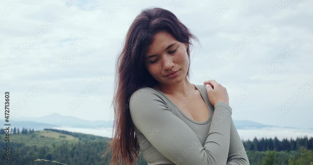 Portrait of young woman with brown hair enjoying time spending on fresh air. Pleasant female in sports clothes relaxing during exercises among green mountains. Portrait of young woman with brown hair enjoying time spending on fresh air. Pleasant female in sports clothes relaxing during exercises among green mountains.