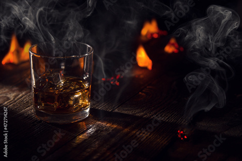 Vászonkép a glass of wiskey on the rocks on a wooden table on the fire