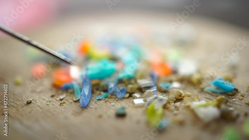 Global ocean pollution concept with microplastics bits and pieces from single-use plastic consumer items. Selective focus of a person examining micro plastics with a pen.