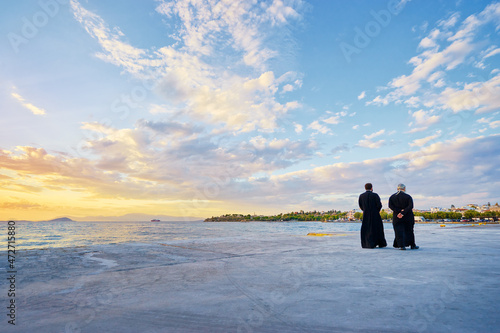 Εκτύπωση καμβά Two priests walking on the sea promenade with wonderful sunset view