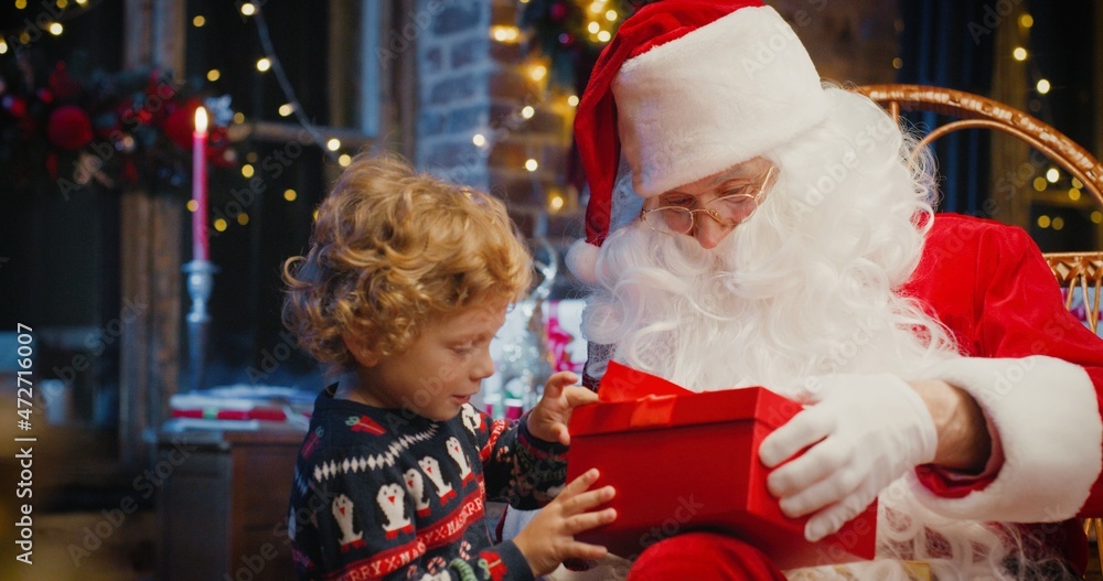Santa Claus and little caucasian boy standing nearby and waiting for magical Christmas gift near the Christmas tree in cozy living room in winter Santa Claus and little caucasian boy standing nearby and waiting for magical Christmas gift near the Christmas tree in cozy living room in winter