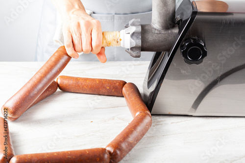 a woman cook wearing apron is stuffing homemade sucuk or sausage into casing using an electrical meat grinder and stuffer. This is an healthier preservative free alternative for these delicious food.