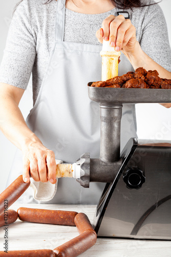 a woman cook wearing apron is stuffing homemade sucuk or sausage into casing using an electrical meat grinder and stuffer. This is an healthier preservative free alternative for these delicious food.