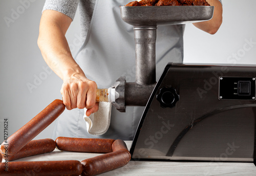 Obraz na plátně a woman cook wearing apron is stuffing homemade sucuk or sausage into casing using an electrical meat grinder and stuffer