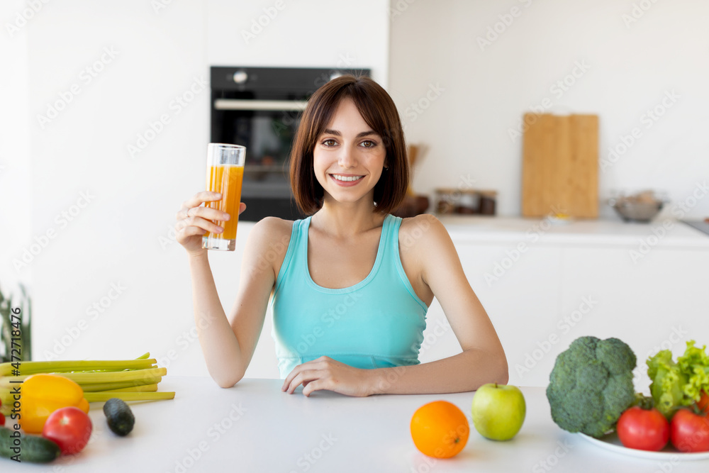 Healthy diet. Happy slim woman drinking orange juice, cooking fresh diner, standing in kitchen and smiling to camera Healthy diet. Happy slim woman drinking orange juice, cooking fresh diner, standing in kitchen and smiling to camera