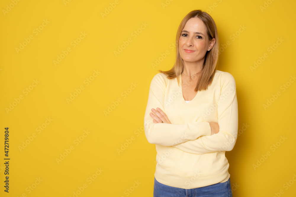 Young smiling woman in casual clothing posing with arms folded isolated over yellow background. Young smiling woman in casual clothing posing with arms folded isolated over yellow background.
