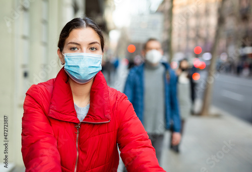Portrait of young woman with brown hair wearing face mask walks along city street