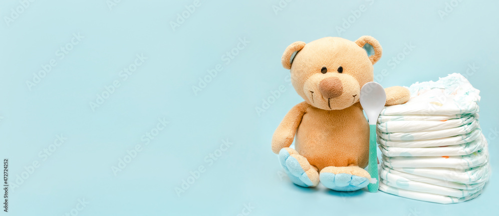 Stack of diapers with cute teddy bear toy on table. set for infant boy girl for baby shower present gift on blue background with copy space. Healthcare medical, hygiene concept
