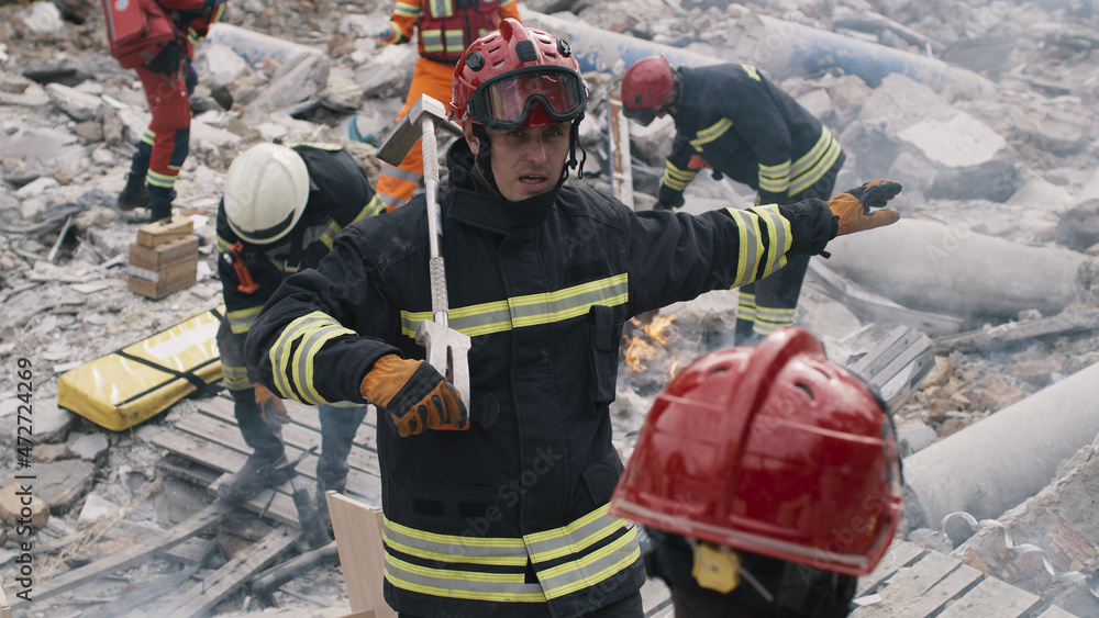 Obraz premium Male emergency workers in uniform talking with each other while working on remains of demolished building after earthquake