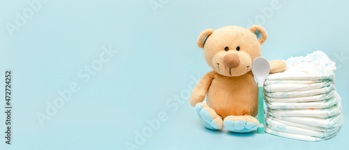 Stack of diapers with cute teddy bear toy on table. set for infant boy girl for baby shower present gift on blue background with copy space. Healthcare medical, hygiene concept
