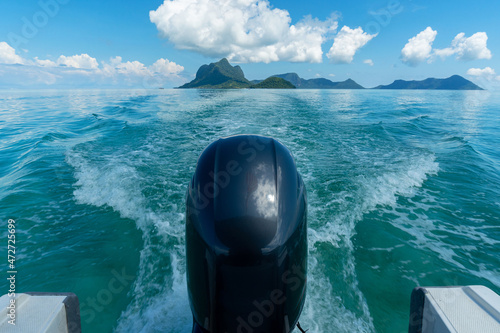 Water trail or boat wake in the waters of Semporna against the backdrop of cloudy blue skies over the islands of Boheydulang, Bodgaya and Tetagan. photo