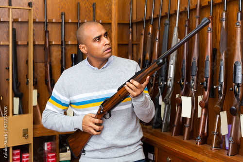 Portrait of ordinary confident man in gun shop showing rifle