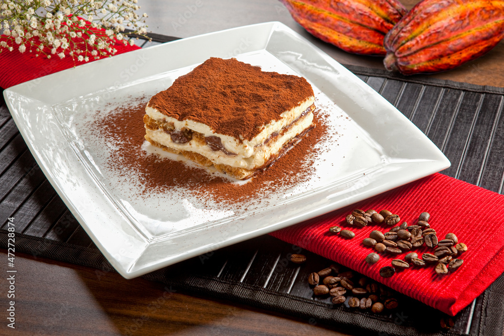 Φωτογραφία Tiramisu em pedaço, típica sobremesa italiana com pó de cacau em prato branco no fundo de mesa