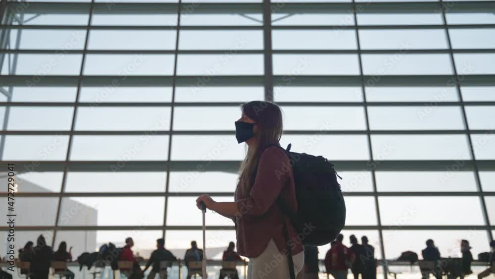 A young woman in a mask waiting for her flight, big airport terminal windows on the background. A young woman in a mask waiting for her flight, big airport terminal windows on the background.