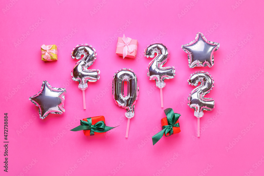 Composition with figure 2022 made of silver balloons and gift boxes on color background Composition with figure 2022 made of silver balloons and gift boxes on color background