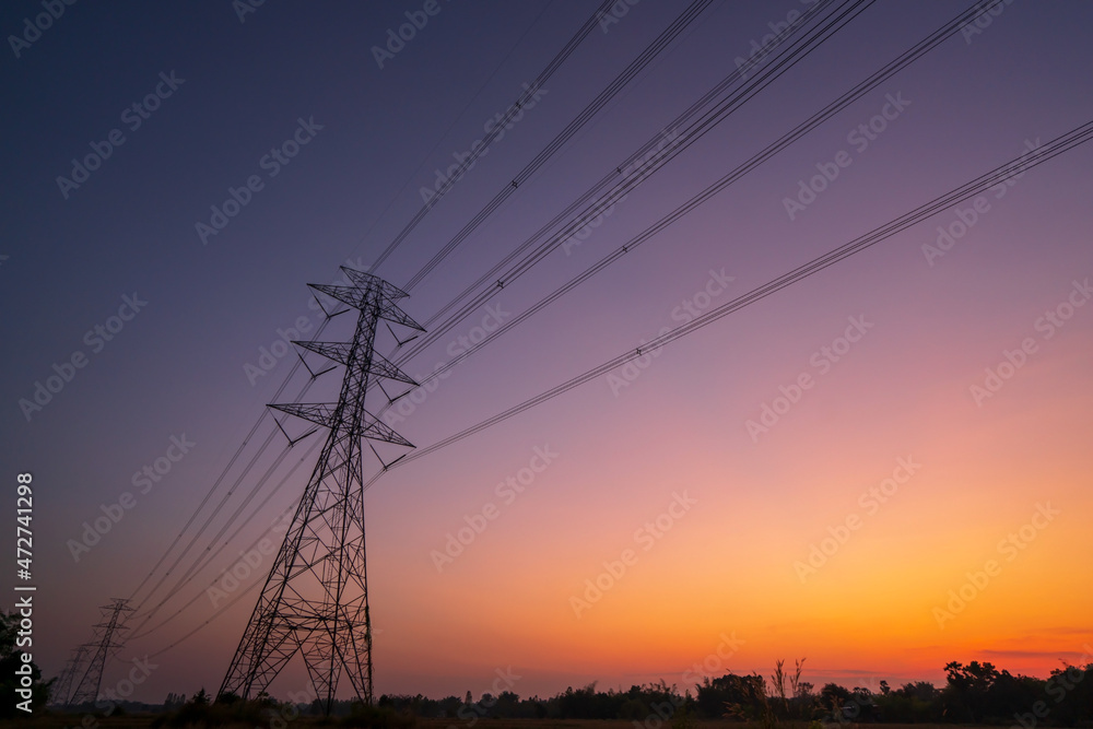 A high voltage tower electric power transmission pole and cable line picture with sunset sky