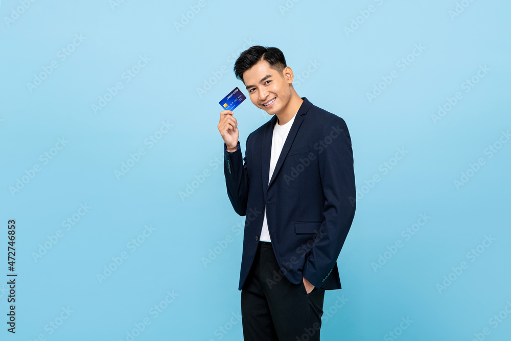 Portrait of happy handsome southeast Asian man in semi formal blazer holding credit card in light blue isolated studio background Portrait of happy handsome southeast Asian man in semi formal blazer holding credit card in light blue isolated studio background