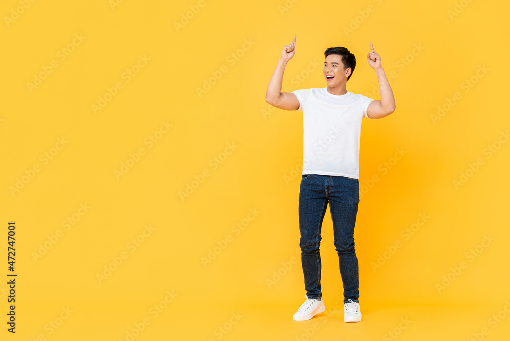 Smiling young handsome Asian man looking at empty space and pointing two fingers upward isolated on yellow studio background Smiling young handsome Asian man looking at empty space and pointing two fingers upward isolated on yellow studio background