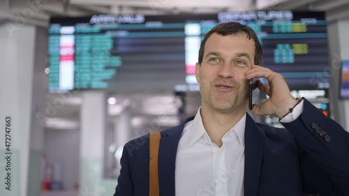 Wallpaper Mural Tourist traveler happy smiling man using mobile phone of flight plane arrivals board timetable in airport terminal for trip travel, Businessman talking on smartphon for check-in. Technologies business Torontodigital.ca