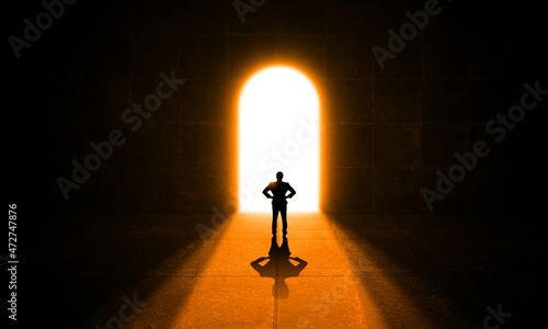 Confident Businessman Standing in front of a Bright Light Door in a dark grungy concrete Hall. Business man Stands alone Looking at open shiny Gate. Confidence, success, Dream and opportunity concept 