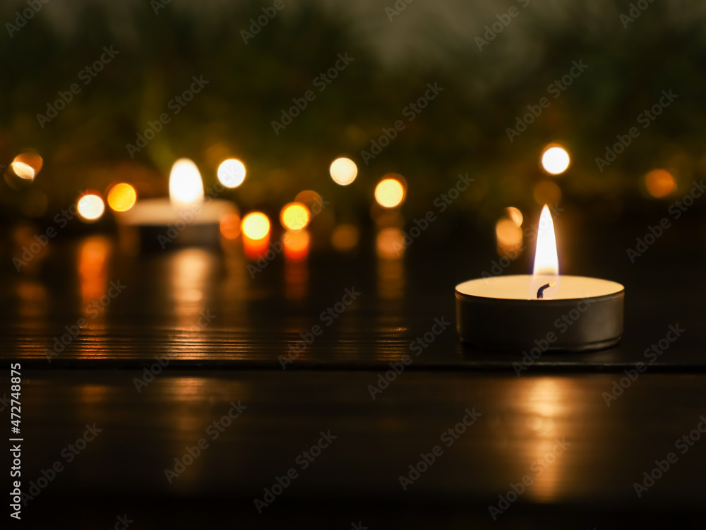 Christmas burning candle on dark wooden table, close up of flame with copy space. Fir Xmas tree texture, bokeh blurred fairy lights in dark night background