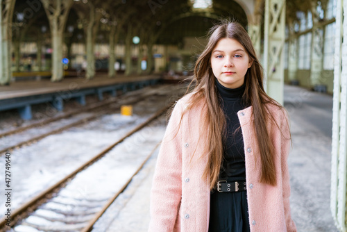 Beautiful young casual tourist woman with a suitcase in a pink coat waiting for a train at the train station. Travel and trip, vacation and tourism, vacation and other concepts. Great pastime © Екатерина Переславце