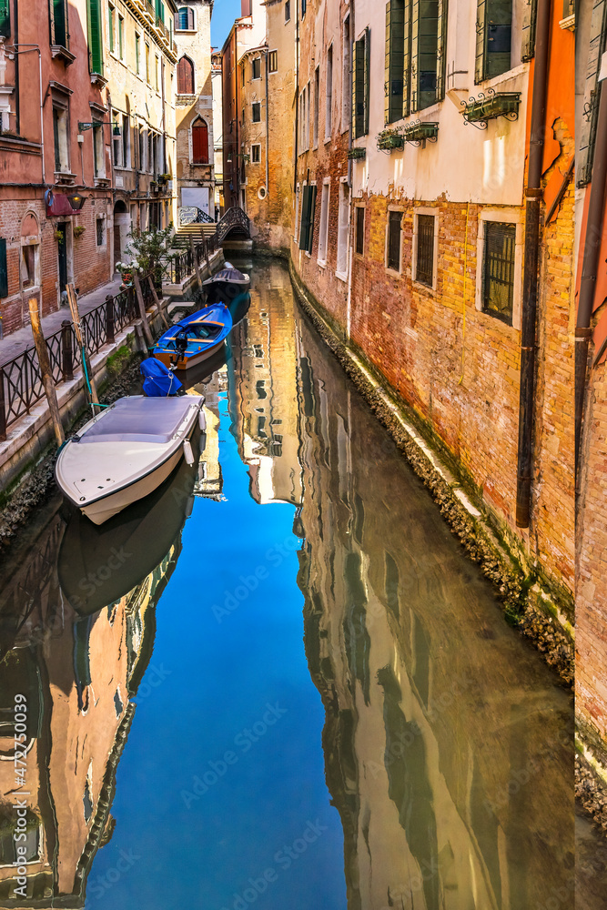 Colorful small canal and bridge creating beautiful reflection in Venice, Italy.
