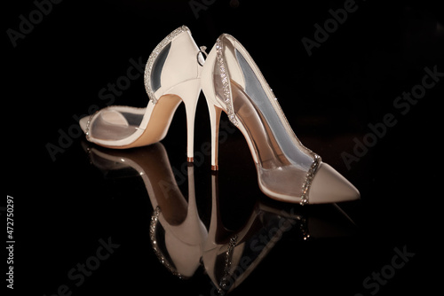 Beautiful white bride's shoes and golden wedding ring on dark table background, copy space. Wedding concept