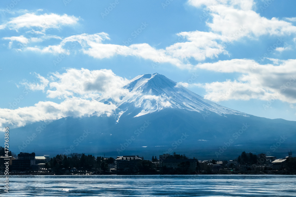 An idyllic view on Mt Fuji from the side of Kawaguchiko Lake, Japan. The mountain is surrounded by clouds. Serenity and calmness. The top of the volcano is covered with snow. Calm surface of the lake.