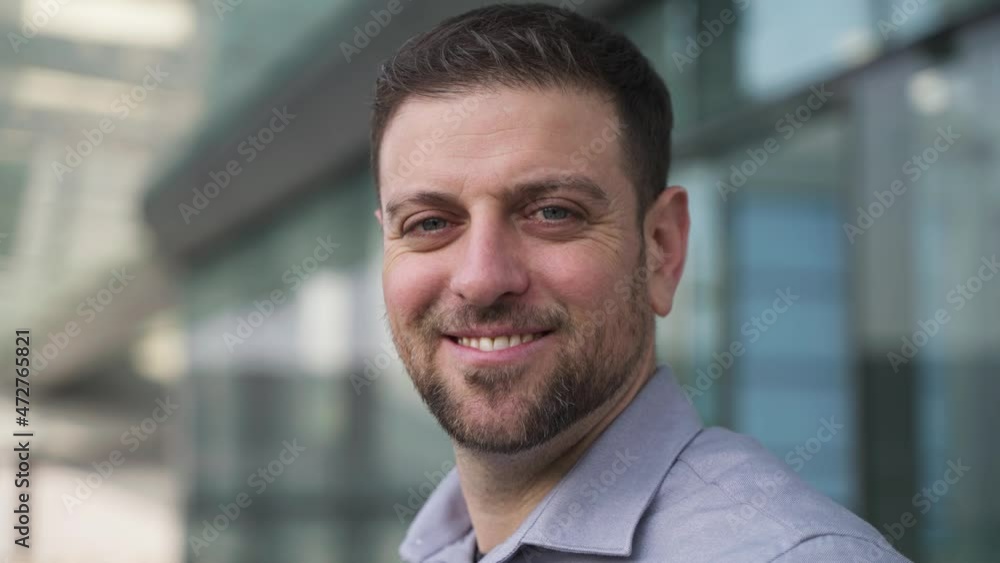 middle age confident beared businessman stands in front of the office building, turns head looking at camera smiles Portrait of successful businessman middle age confident beared businessman stands in front of the office building, turns head looking at camera smiles Portrait of successful businessman