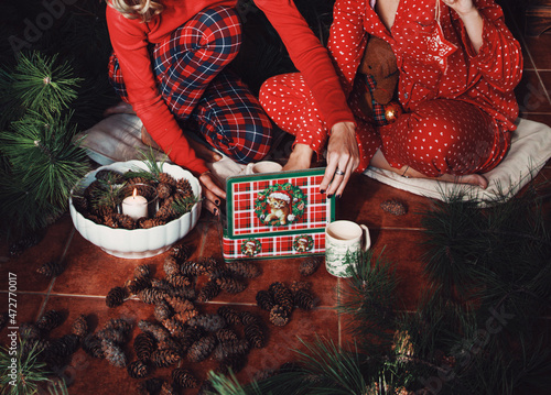Two young women in red pajamas opening cookie's box, december morning, christmass decoration