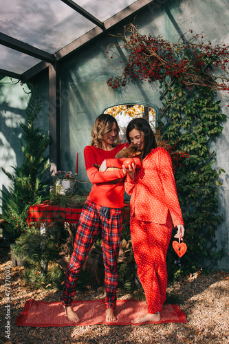 Two young women in red pajamas holding kitten, december morning, christmass decoration