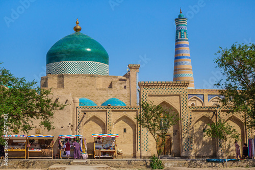 Two of main attractions of Khiva (Uzbekistan): Islam Khodja minaret and Pahlavan Mahmoud mausoleum with unique green dome. Merchants sell and tourists walk by walls below photo