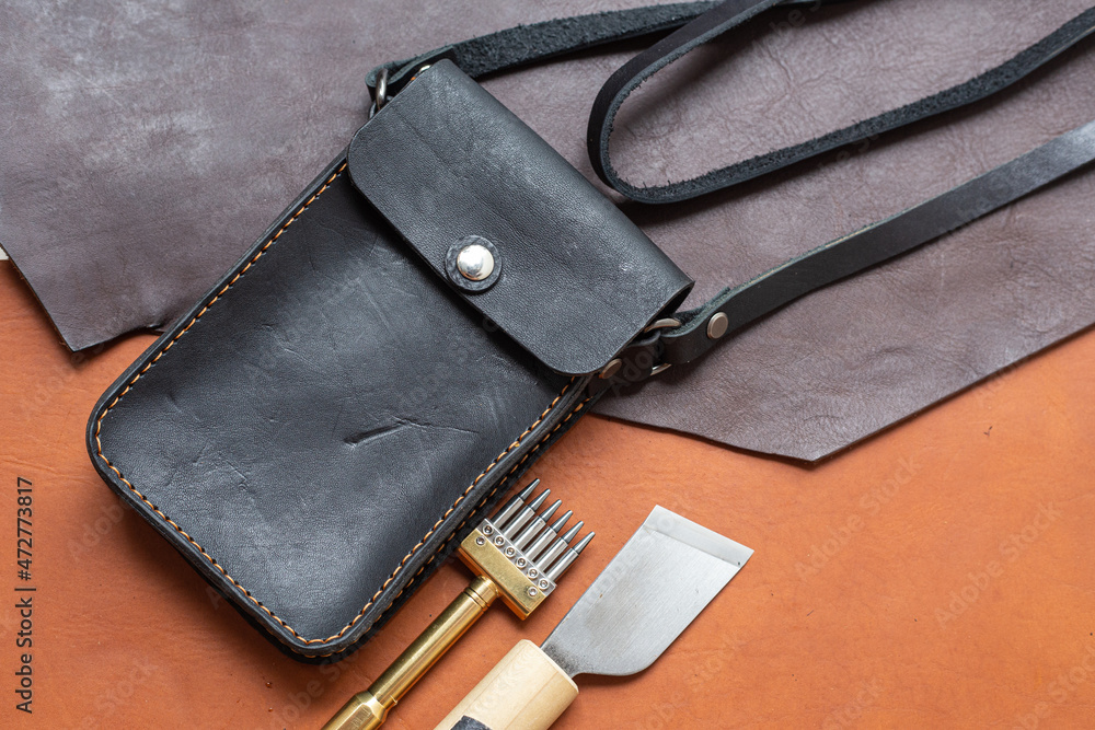 Leather phone and wallet bag working with tool on leather background Leather phone and wallet bag working with tool on leather background