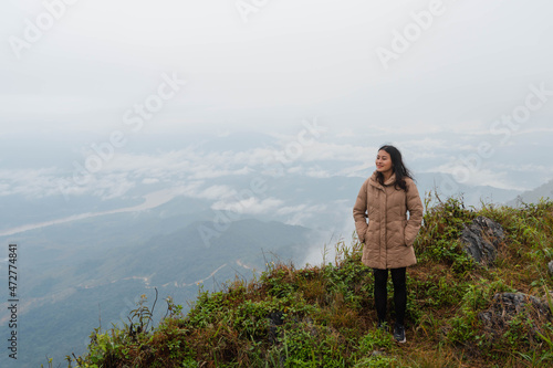 happy Asian woman in winter coat standing on mountain peak at Pha Tang view point 103 with river view and sea mist and heavy fog sky. travel place in Chaing Rai  Thailand